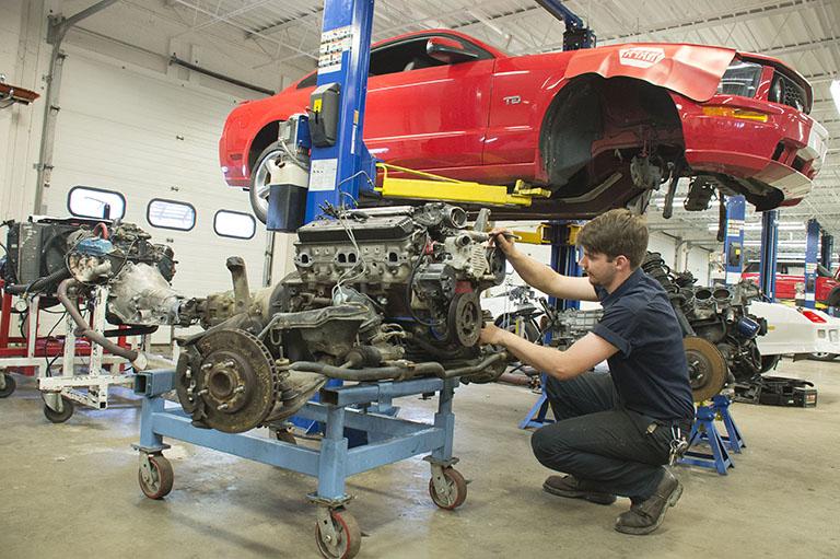 An automotive technology major working on the engine of a red vehicle